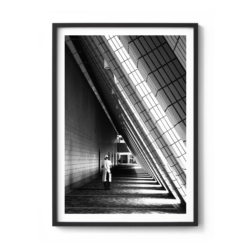 Framed black and white photo of a person standing in a long, narrow hallway with high ceilings.